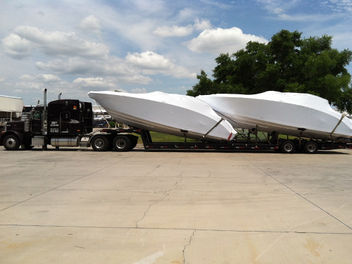 Two shrink wrapped boats secured to a semitruck bed for transport