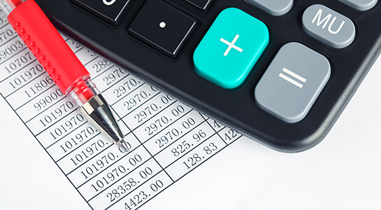 On a spreadsheet listing dollar amounts, a calculator and red pen sit ready for use.