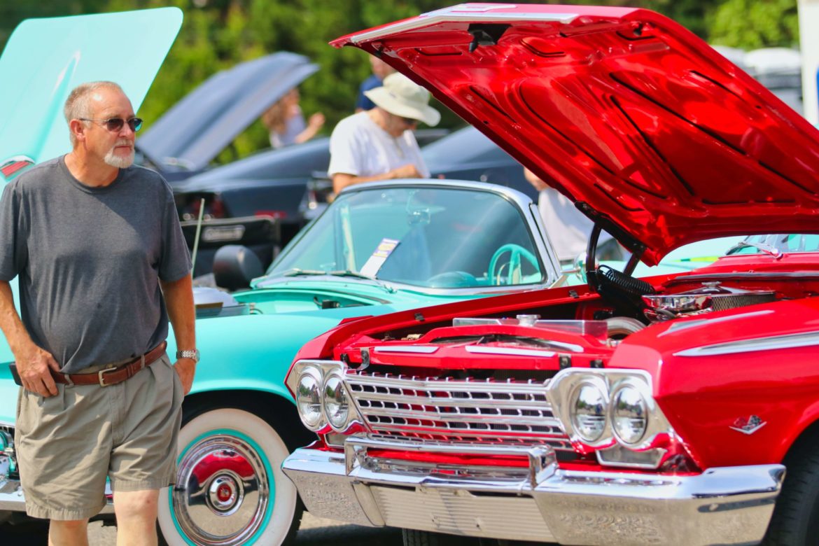 A car show attendee walking past a car on display with its hood up