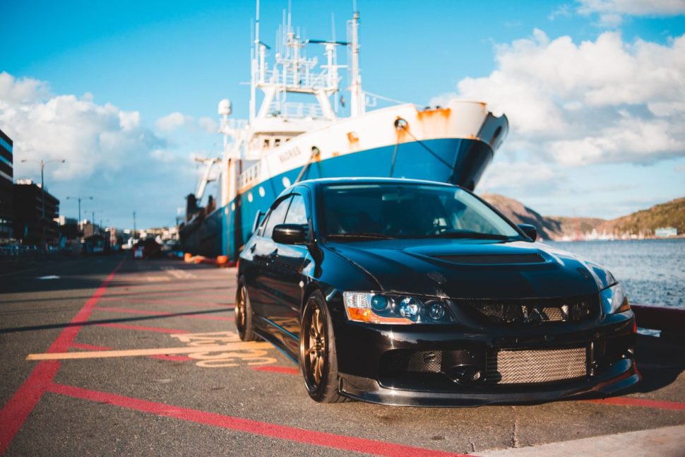 Photo of a luxury car in front of a freight ship